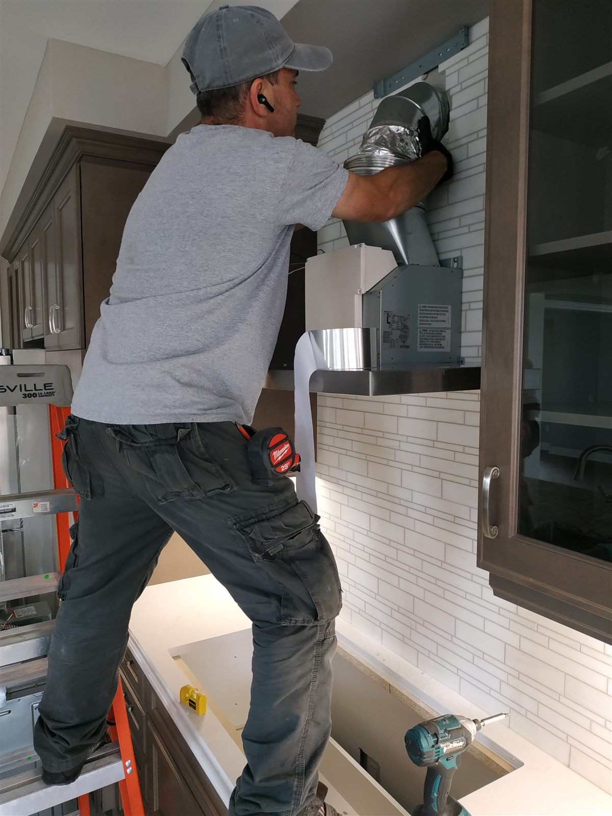 Technician installing a kitchen range hood and duct connection